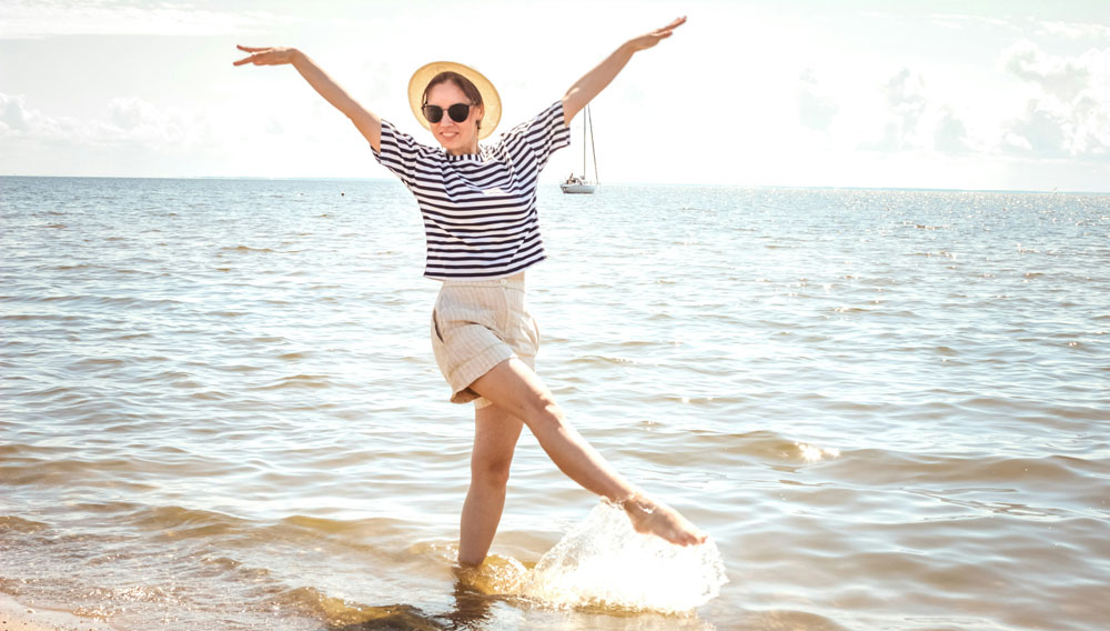 Frau steht am Sandstrand mit den Füßen im Meer (Timur M auf Unsplash)