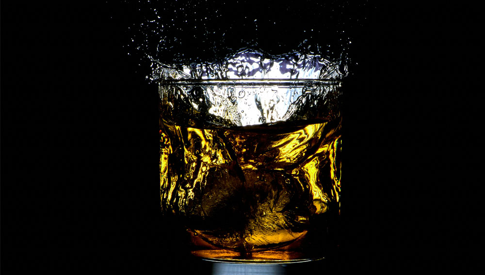 Flüssigkeit spritzt aus einem Glas vor schwarzem Hintergrund (Foto: Mathew Schwartz auf Unsplash)