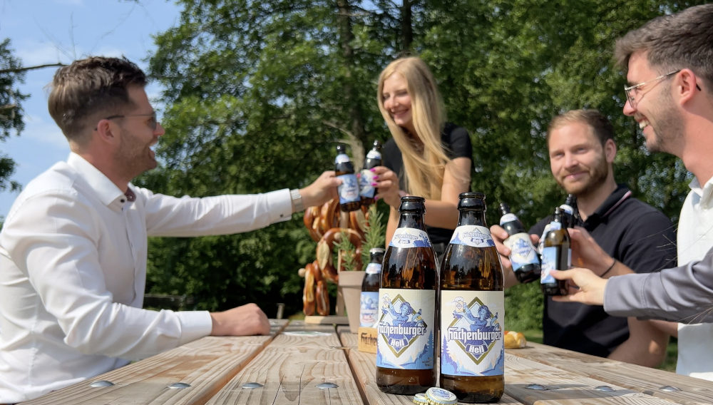 Menschen an einem Tisch im Freien stoßen mit Bierflaschen an