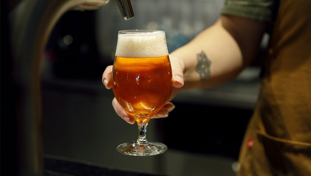 Hand hält frisch gezapftes Bier (Foto: Urban Gyllström auf Unsplash)