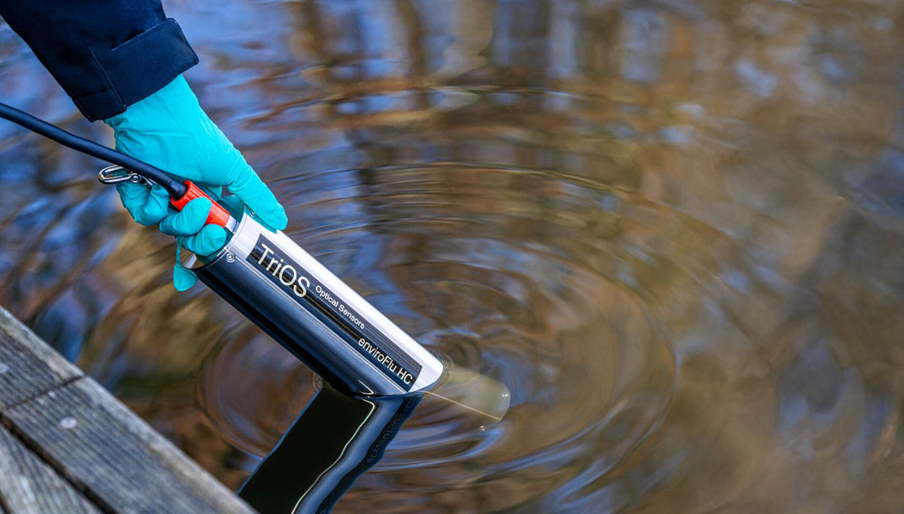 Eine Person misst die Wasserqualität mit einem Sensor von TriOS