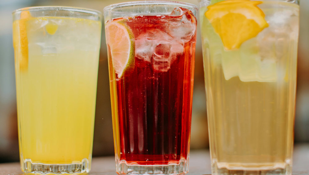 Drei Gläser mit verschiedenen Kaltgetränken und Eiswürfeln auf einem Tisch (Foto: Eliano Davide auf Unsplash)